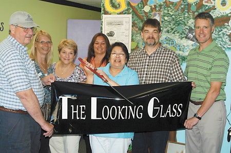 Mayor Pro Tem Leon Laylin, Mary Cooper of Leader Publications, Sandie Judd of Judd Lumber, Kim MacGregor of Edward Jones, husband, Joe Gray, and state Sen. John Proos gather around Connie Gray as she snips The Looking Glass banner July 11.